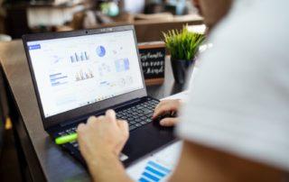 Foto de um notebook com gráficos na tela e mão de um homem branco sobre o teclado para simbolizar a contabilidade digital