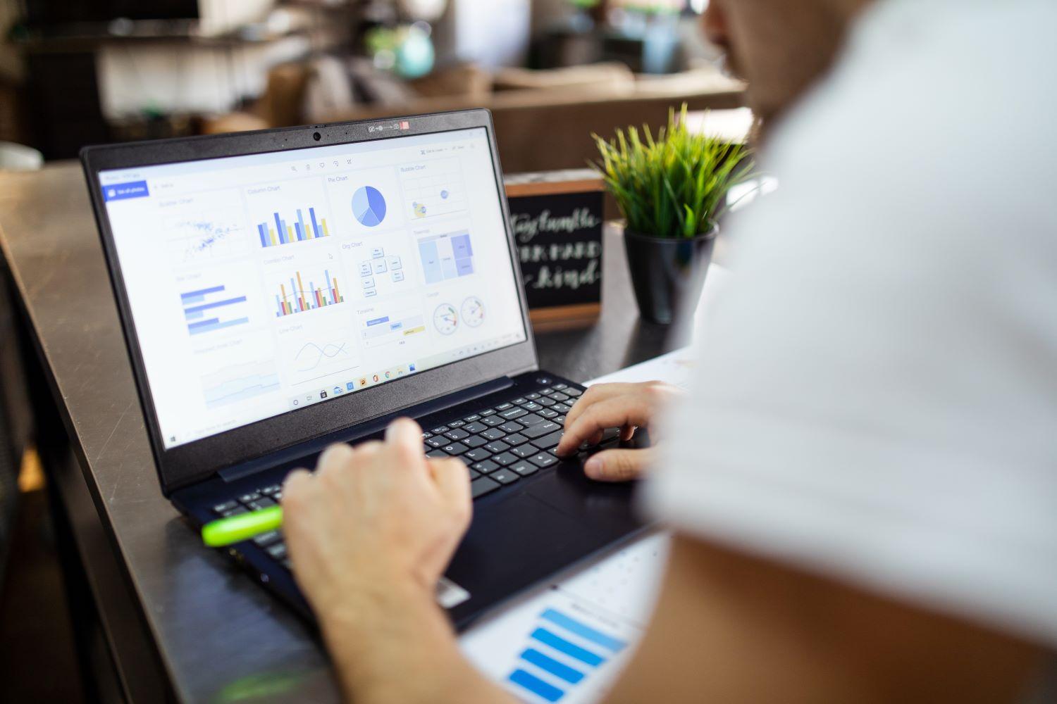 Foto de um notebook com gráficos na tela e mão de um homem branco sobre o teclado para simbolizar a contabilidade digital